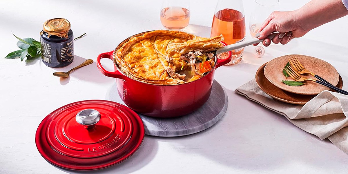 Le Creuset Round Dutch Oven next to lid with person stirring food inside Le Creuset Round Dutch Oven next to lid with person stirring food inside