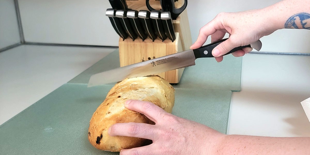 Person using Henckels knife to slice bread Person using Henckels knife to slice bread