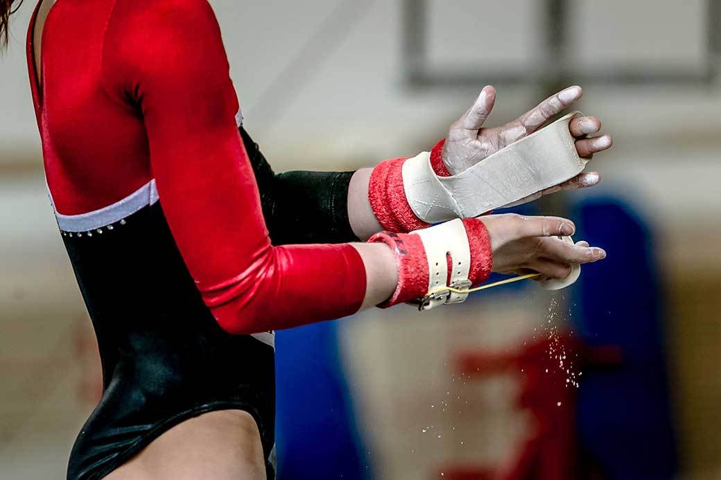 A gymnast wearing hand grips chalks their hands.