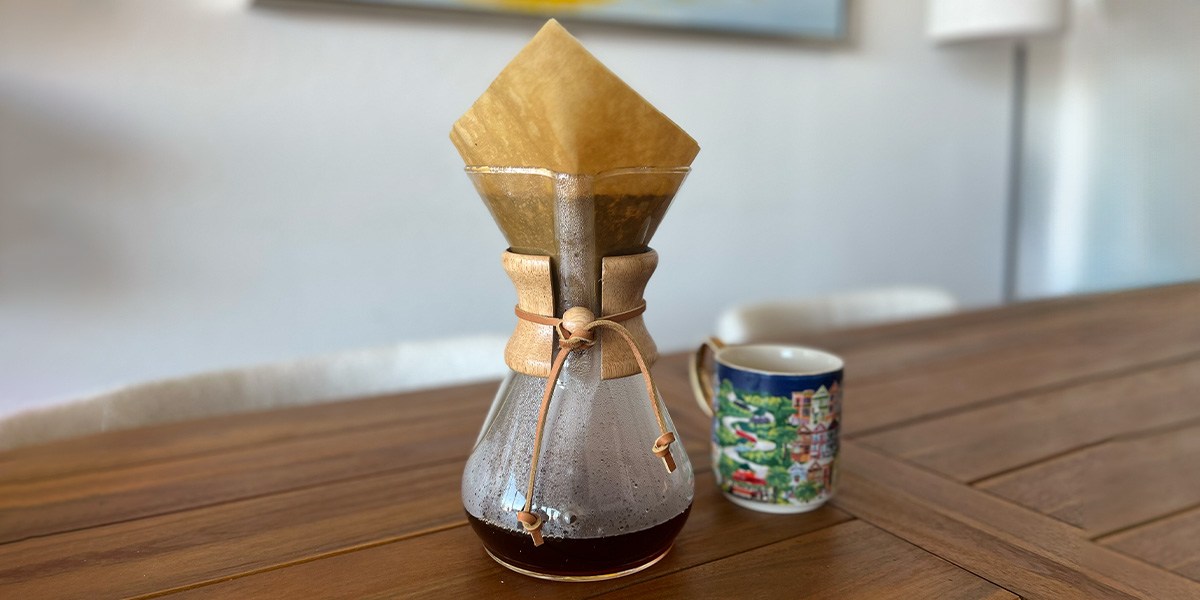 Chemex Pour-Over Glass Coffee Maker next to coffee cup on table