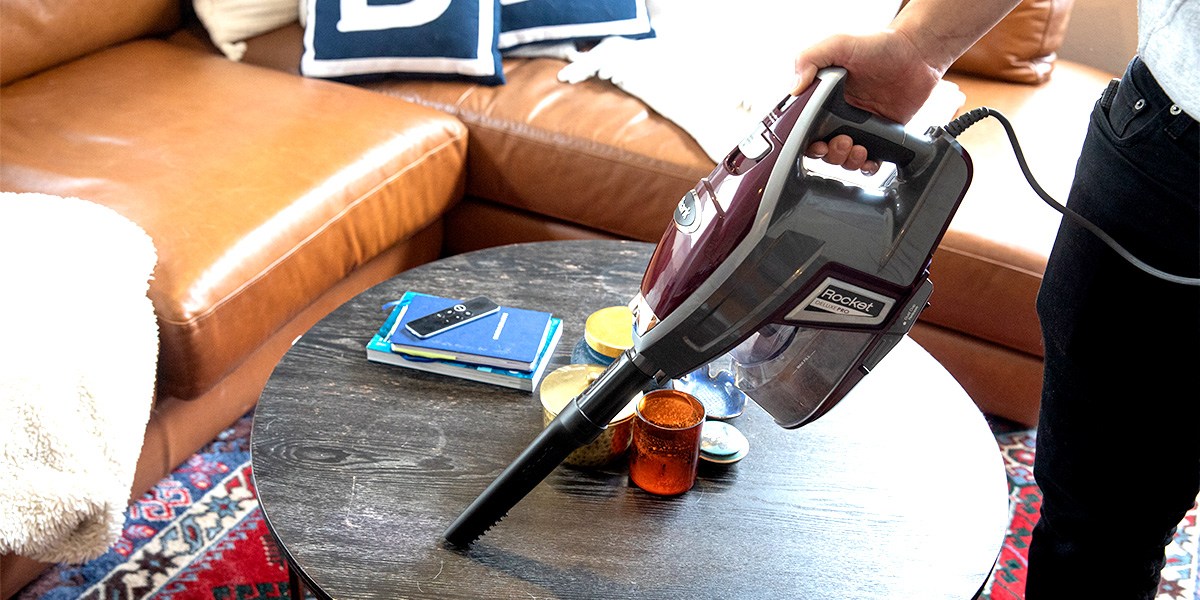 Person using Shark Rocket Pet Vacuum to clean coffee table